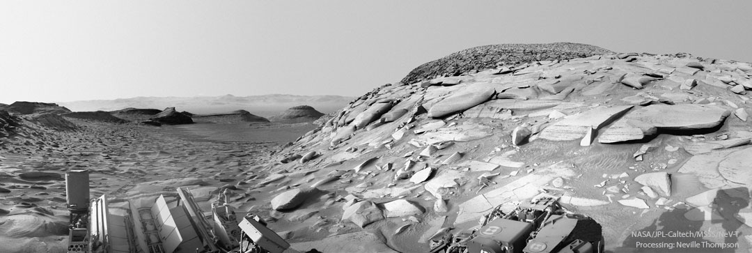 Das Schwarzweiß-Bild zeigt einen Hügel auf dem Mars, der mit plattenartigen flachen Felsen bedeckt ist.