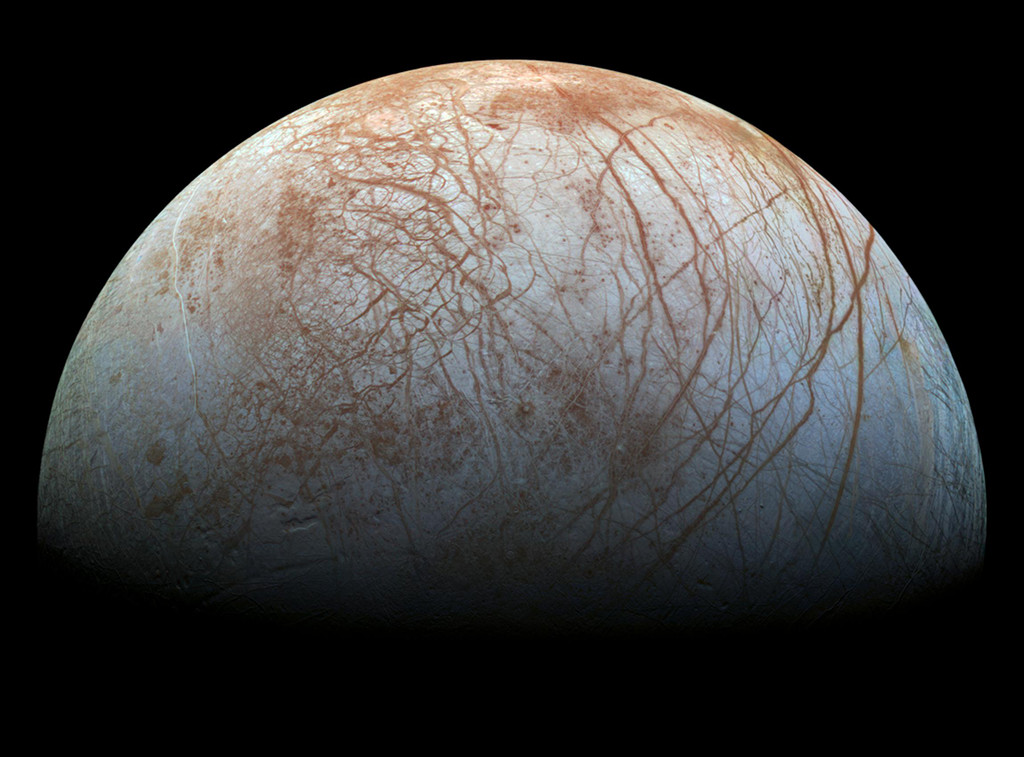 Das Bild zeigt den von oben zur Hälfte beleuchteten Jupitermond Europa, er ist von langen rötlichen breiten Furchen überzogen, die auf der rechten Seite sehr lang sind und links eher wie ein Spinnennetz wirken.