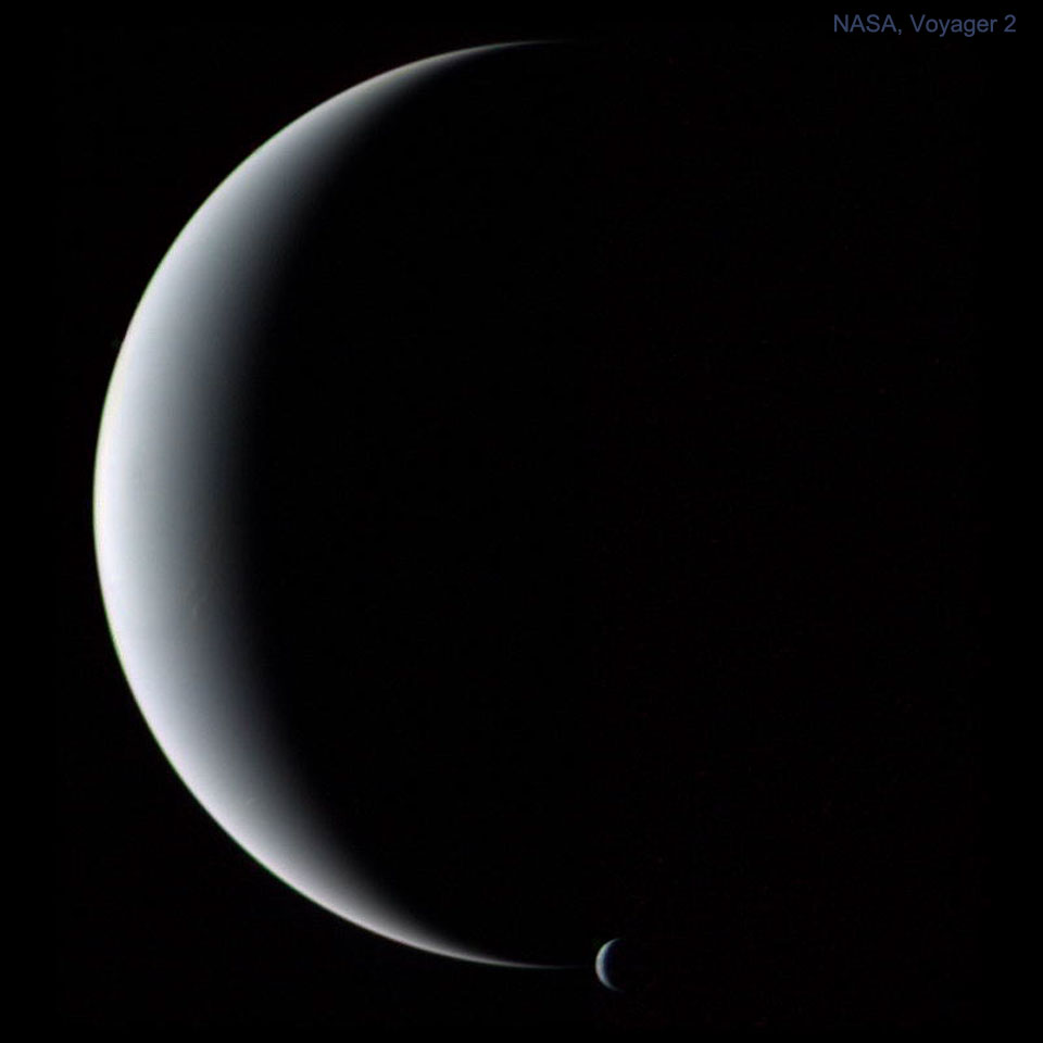 Das Bild zeigt eine große Sichel des Planeten Neptun, die Schattengrenze ist diffus verschwommen. An der unteren Spitze der Sichel befindet sich eine zweite kleine Sichel, die des Mondes Triton.