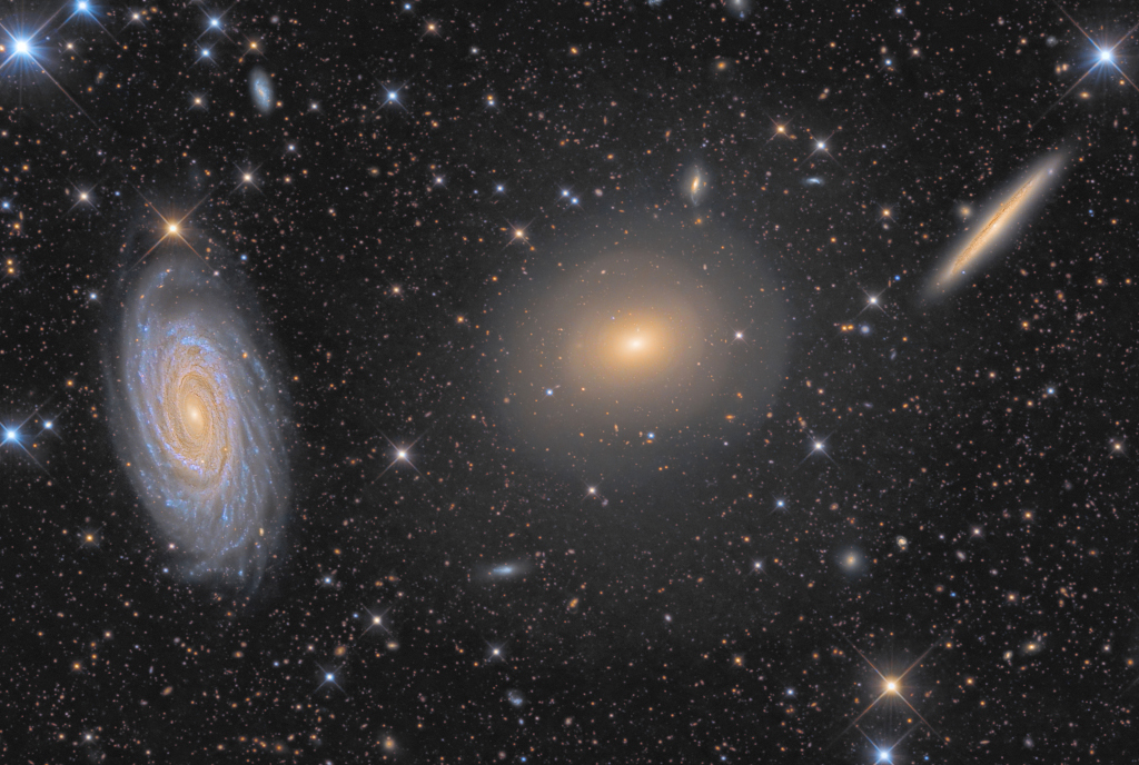 Drei Galaxien in einer Reihe, die linke hat eine ausgeprägte Spiralstruktur und ist schräg von seitlich oben zu sehen, die mittlere ist elliptisch fast ohne Struktur, und die rechte ist von der Kante zu sehen und daher sehr schmal.
