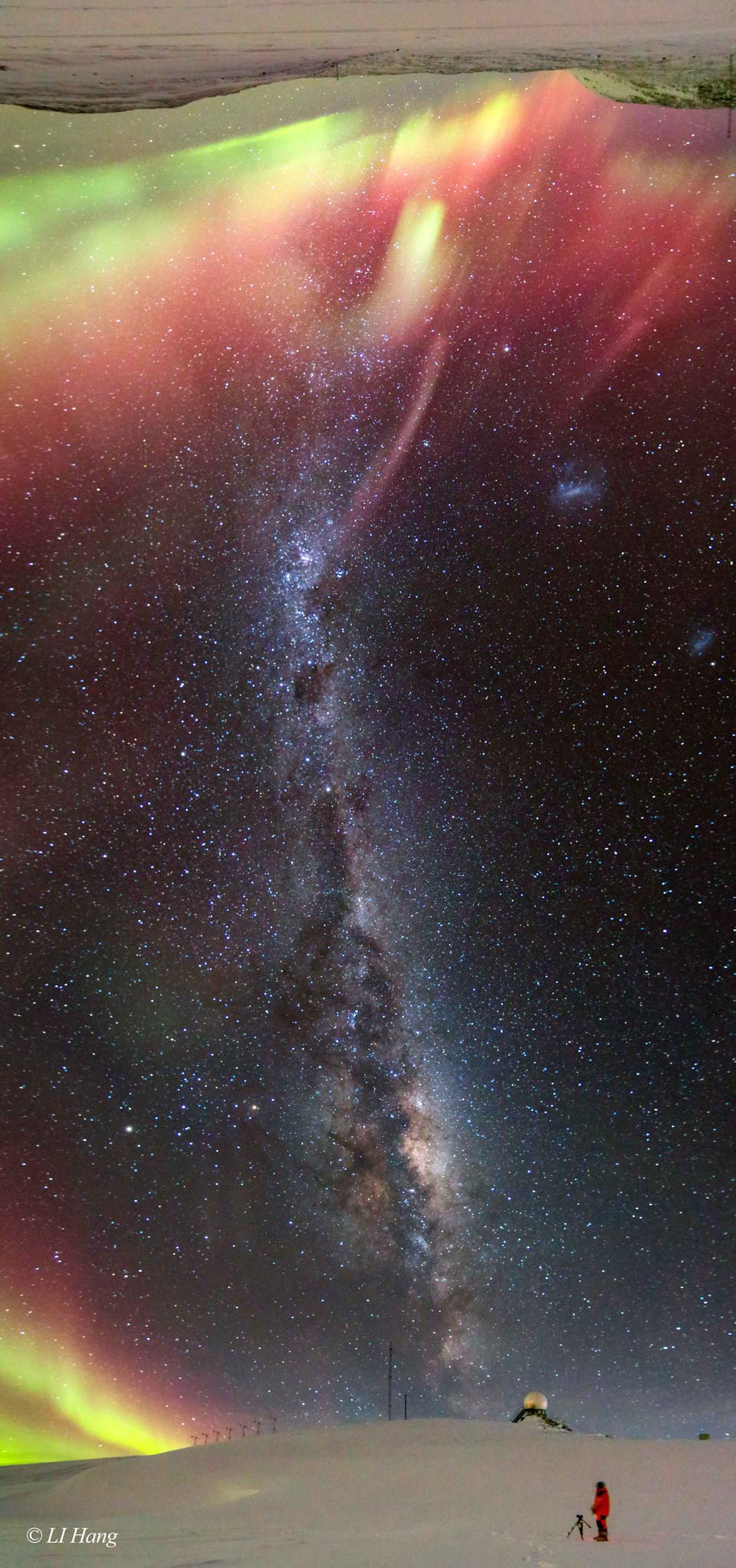 Das Panorama zeigt ein Himmelsband von Horizont zu Horizont einer verschneiten Landschaft. Die Milchstraße mit Dunkelwolken verläuft entlang des Bildes, an den Horizonten oben und unten leuchten Polarlichter.