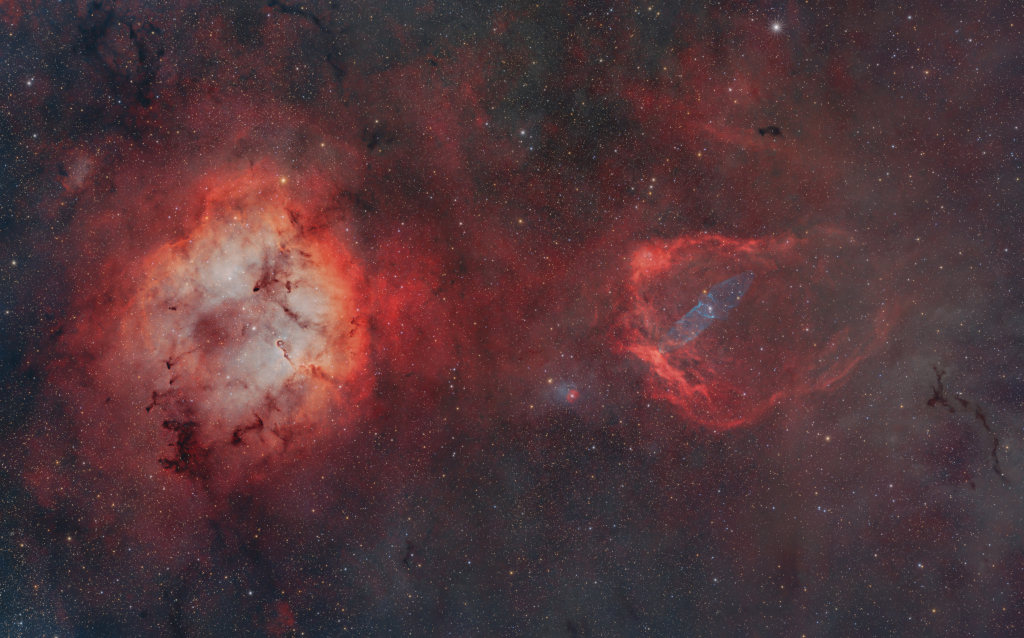 Links leuchtet eine runde helle Emission mit rötlichem Rand, rechts ein weniger heller roter Wulst mit einem schwach leuchtenden bläulichen Inneren.