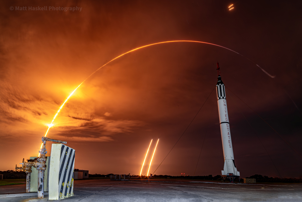 Im Vordergrund steht rechts eine Rakete, links hinten zieht der Bogen einer startenden Rakete nach rechts, und in der Mitte verlaufen zwei kurze Leuchtspuren. Auch am oberen Bildrand sind zwei sehr kurze Leuchtspuren zu sehen.