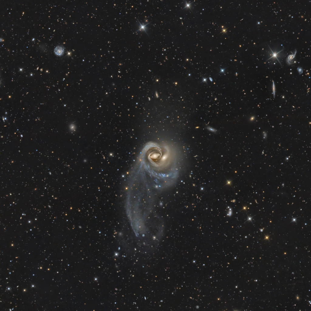 Von Sternen und Galaxien umgeben schweben mitten im Bild zwei ausgeprägte Spiralen, die so eng verschlungen sind, dass sie auf den ersten Blick wie eine einzige wirken. Nach rechts unten verläuft ein nebelartiger Schweif abwärts.