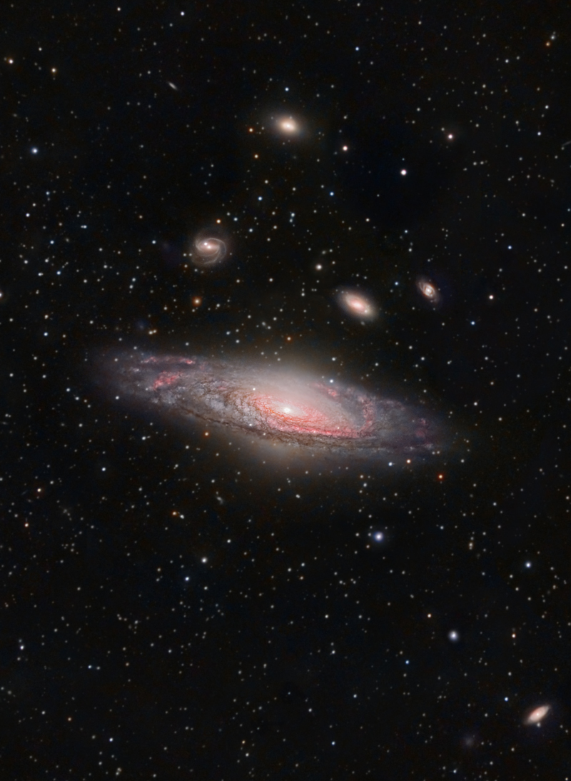 Um eine große Spiralgalaxie, die schräg in der Bildmitte leuchtet, sind mehrere kleinere Galaxien angeordnet.
