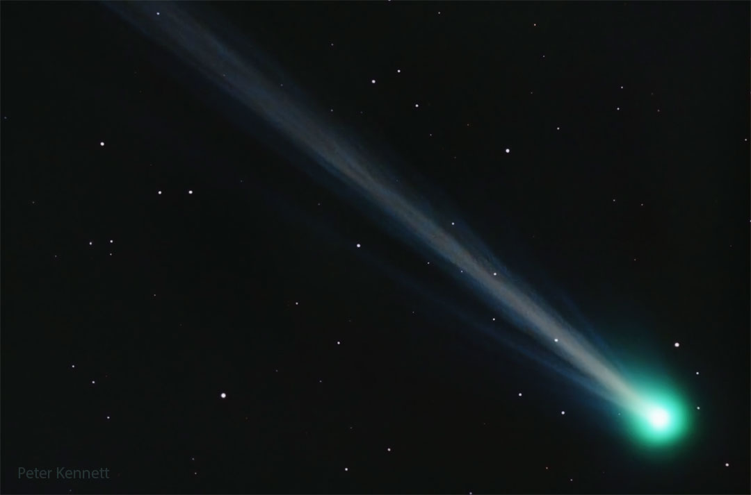 Rechts unten im Bild leuchtet ein Kometenkopf mit grünlicher Koma, der weißliche Schweif verläuft nach links oben.