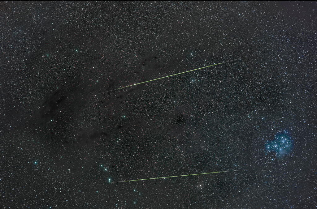Über einen sternbedeckten Himmelsausschnitt zischen zwei Meteorspuren fast waagrecht durchs Bild. Rechts unten ist der kompakte Sternhaufen der Plejaden.