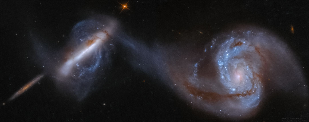 Im Bild sind drei Galaxien zu sehen: Links eine von der Kante, eine zweite ebenfalls von der Kante, aber von Gezeitenschweifen umgeben, und eine dritte Spiralgalaxie rechts von oben.