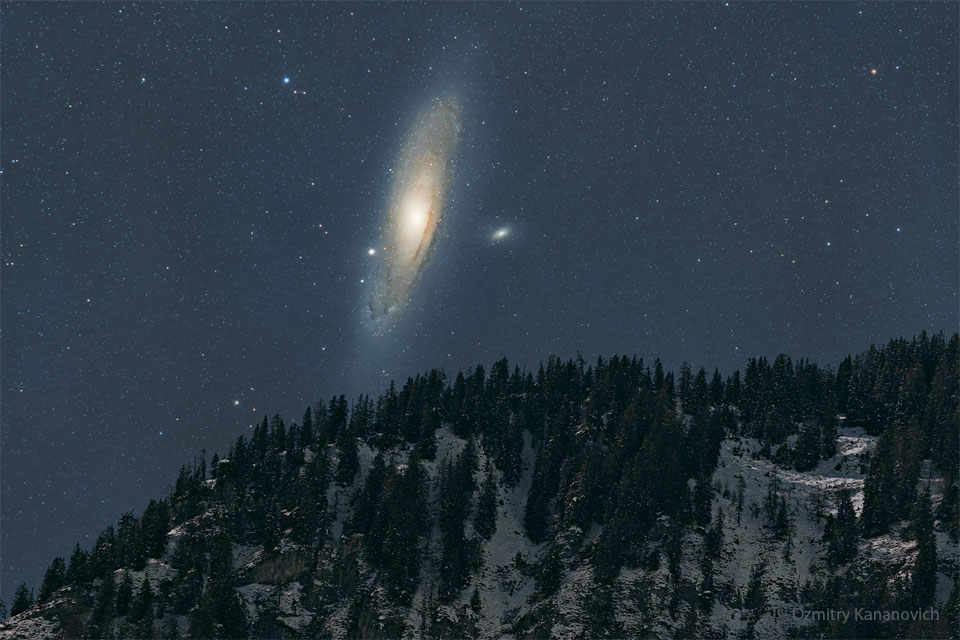 Am Nachthimmel über einem verschneiten Berg leuchtet eine riesige Spiralgalaxie - die Andromedagalaxie.
