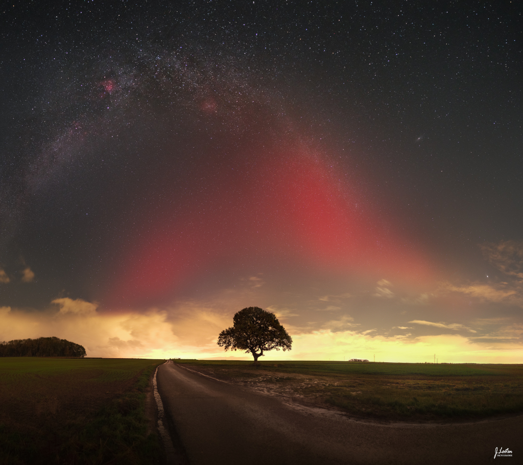 Am Horizont zeichnet sich vor einem hellen Licht die Silhouette eines Baums ab, links steht ein Wald, dazwischen führt ein Weg zum Horizont.
Am Himmel wölbt sich die Milchstraße und ein intensiv rotes Licht.