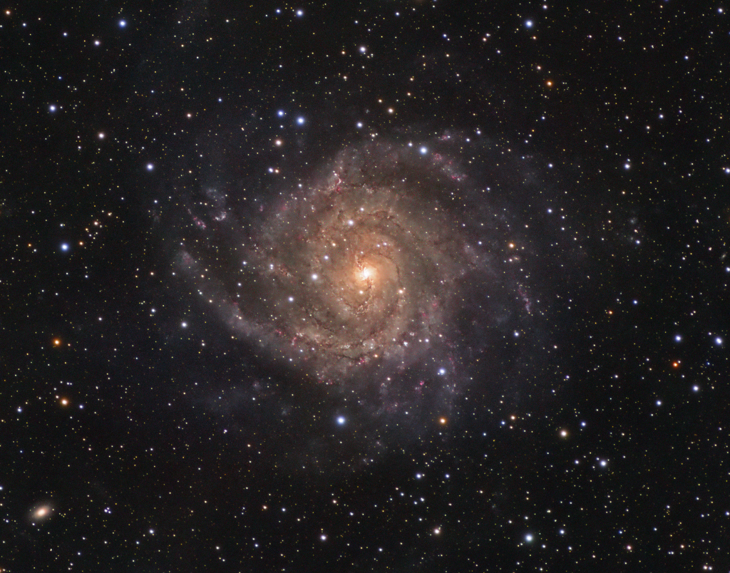 Mitten im Bild ist eine Galaxie direkt von oben sichtbar. In der Mitte ist ein belblicher Kern, der von eng gewundenen Spiralarmen umgeben ist.