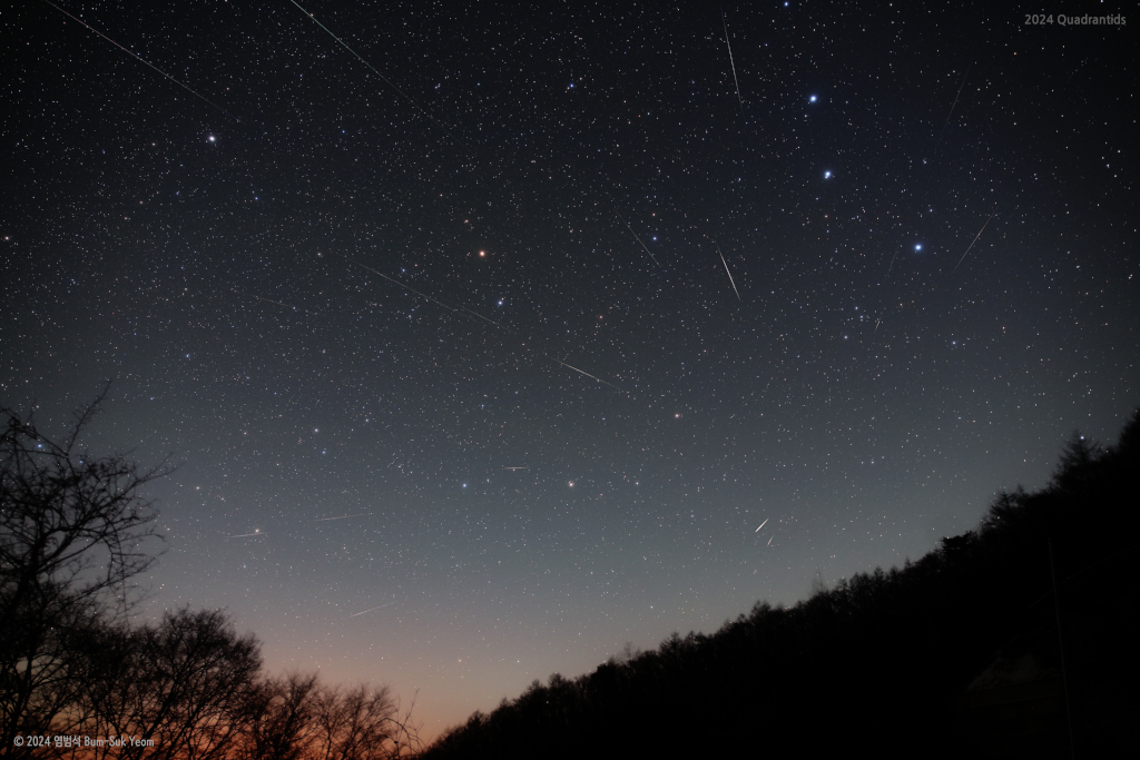 Rechts unten ist die dunkle Silhouette eines bewaldeten Hanges, links unten die Kronen von kahlen Bäumen. Darüber breitet sich ein klarer Sternenhimmel aus. Meteore blitzen durchs Bild, sie strömen von einem Punkt im nicht mehr existierenden Sternbild Mauerquadrant aus. Von oben ragt die Deichsel des großen Wagens ins Bild. Der Mittlere der drei Sterne, Mizar-Alcor, ist ein Doppelstern. Links daneben sind die markanten hinteren Kastensterne des kleinen Wagens, noch weiter links und etwas höher der Polarstern.