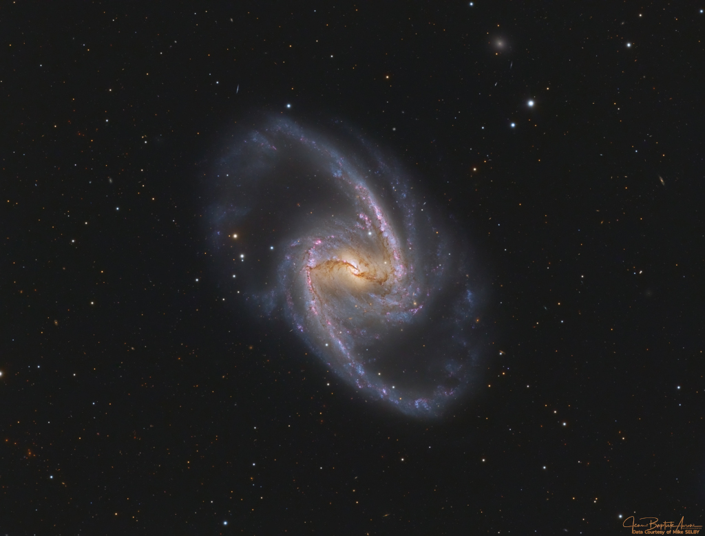 In der Bildmitte schwebt eine Spiralgalaxie mit einem Balken und ausgeprägten Spiralarmen. Über dem Zentrum verlaufen Staubbahnen, an den Spiralarmen sind Sternbildungsgebiete.