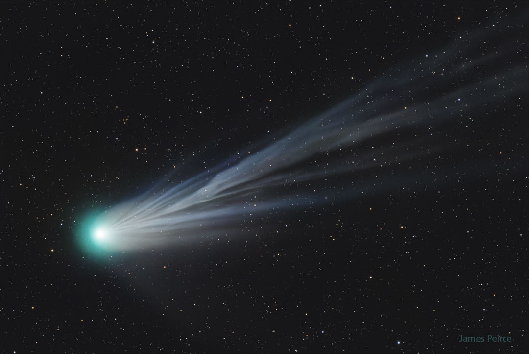 Links strahlt der Kopf eines Kometen, vorne ist er von einer türkis-grünen Koma umgeben, nach rechts oben breitet sich ein langer, stark aufgefächerter Schweif aus.