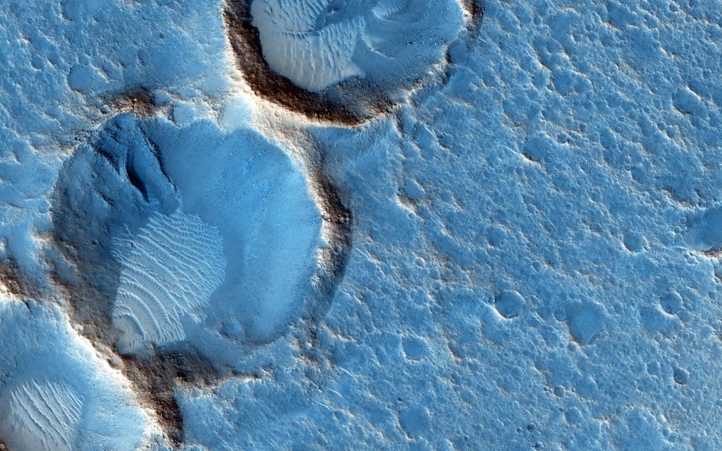 Die Marsoberfäche wurde in Falschfarben-Blau gefärbt. Die Oberfläche erinnert an zerfallenen Seifenschaum, links sind drei tiefe Krater mit Wällen eingegraben, in deren Inneren Ablagerungen liegen.