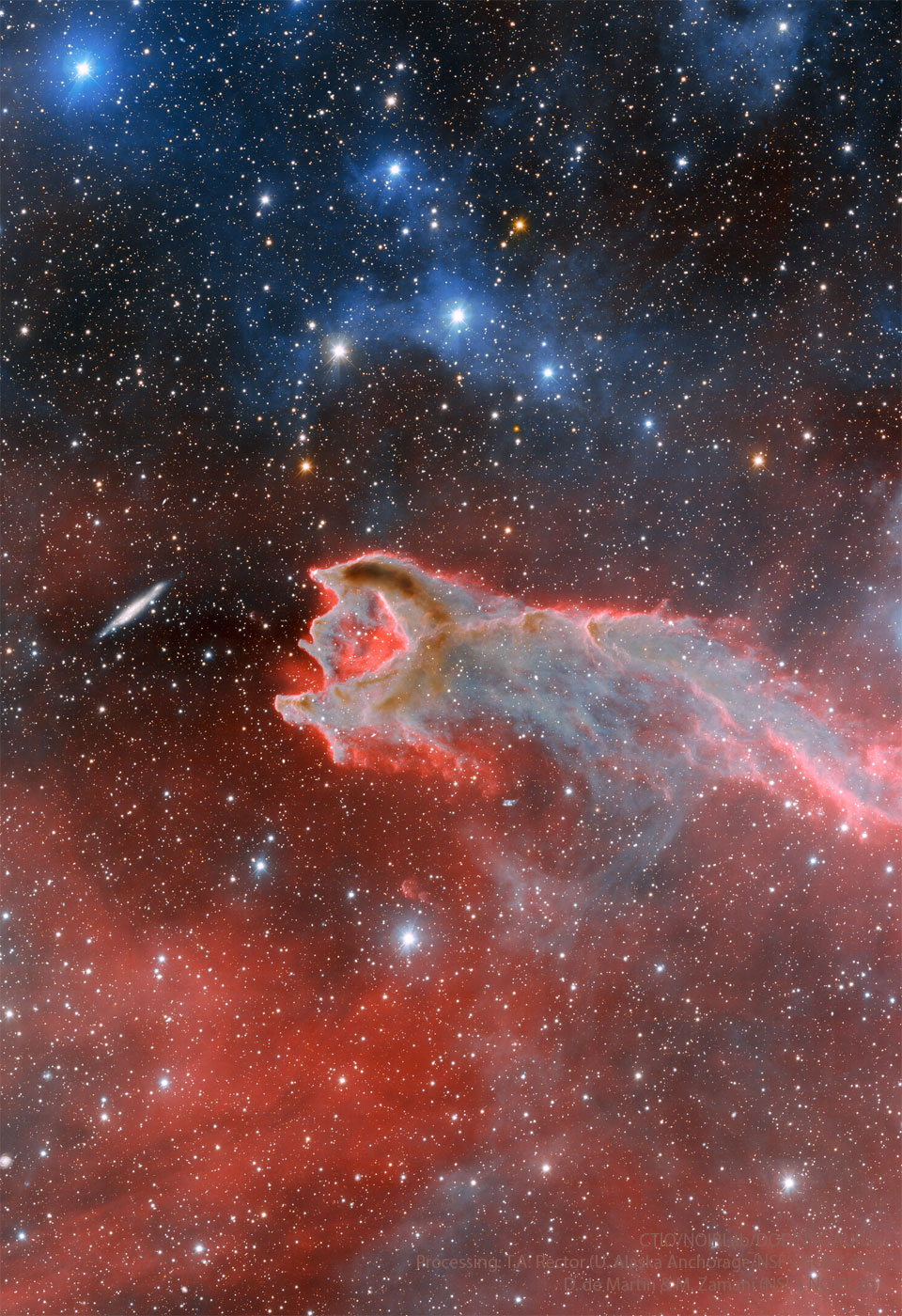 Im Bild schnappt scheinbar eine Staubwolke nach einer Galaxie. Tatsächlich handelt es sich um eine zufällige Anordnung. Die Staubwolke ist von leuchtend roten Nebeln umgeben, das Bild ist voller Sterne.