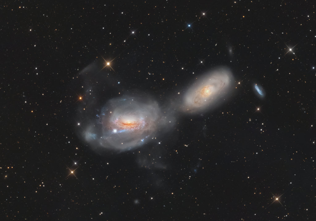 Mitten im Bild leuchten zwei verschwommen wirkende große Galaxien. Beschreibung im Text.