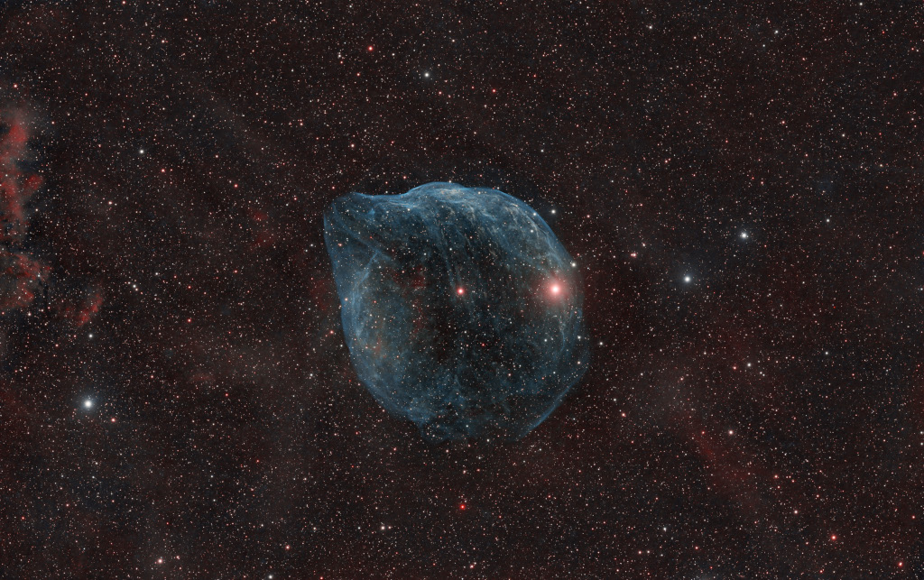 Der blasenförmige, blau leuchtende Nebel im Bild wirkt zart und fragil, seine Form erinnert an den Kopf eines Delfins.