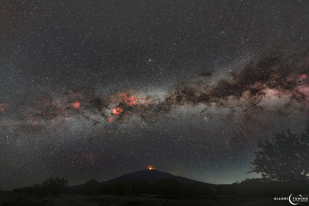 Rotes Licht leuchtet in der Milchstraße und auf dem Berg auf der Erde, dem Schichtvulkan Ätna auf der italienischen Insel Sizilien.