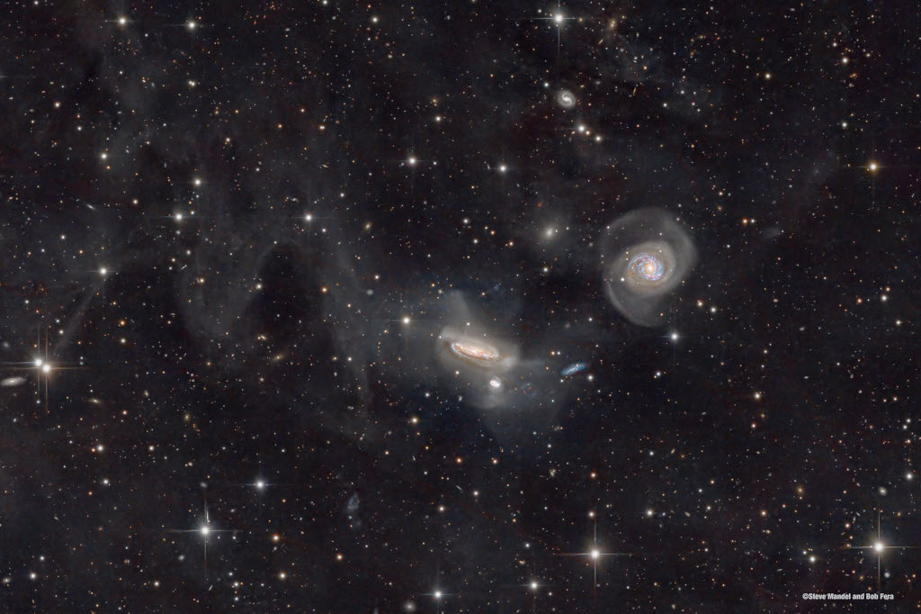 Hinter dicht verteilten Sternen sind mehrere Galaxien zu sehen. In der Mitte sind zwei stark verzerrte Spiralgalaxien mit Hüllen.