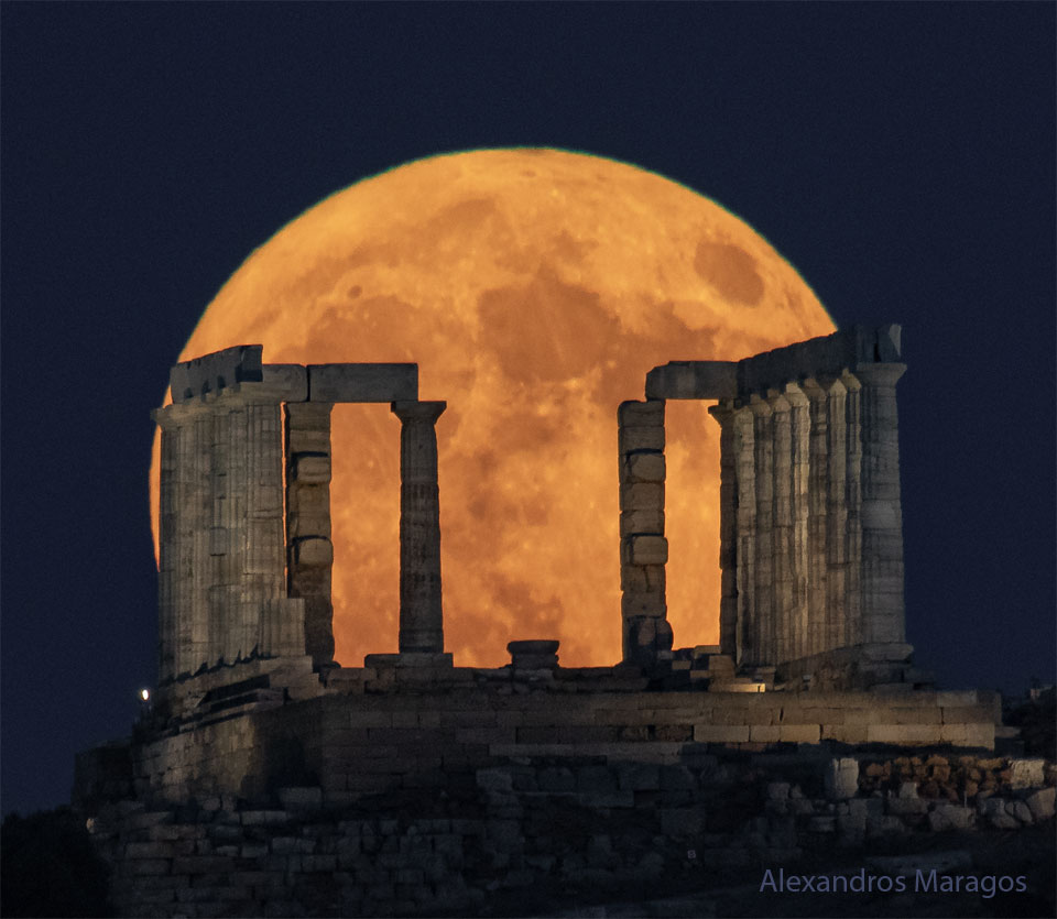 Der volle Supermond geht hinter dem Tempel des Poseidon auf dem griechischen Kap Sounion auf. Er leuchtet orangefarben hinter den Säulen des Tempels.
