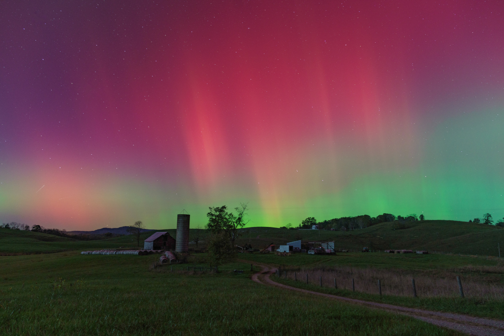 Über einer dämmrigen Landschaft leuchten Polarlichter am ganzen Himmel. Unten sind sie grün gefärbt, oben purpurfarben.