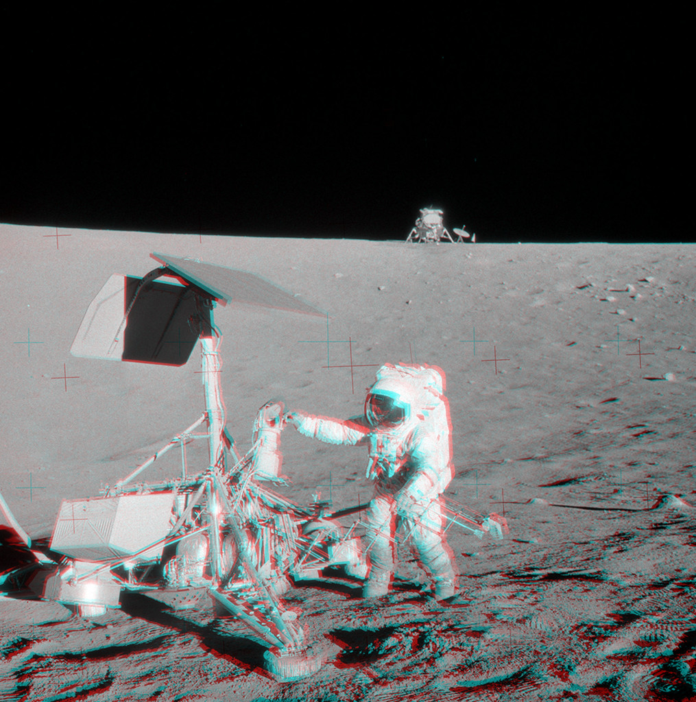 Mit rot-blauen Brillen wirkt das Bild dreidimensional. Die Anaglyphe zeigt einen Astronauten bei einer Raumsonde auf dem Mond. Hinten am Horizont steht die Mondlandefähre.