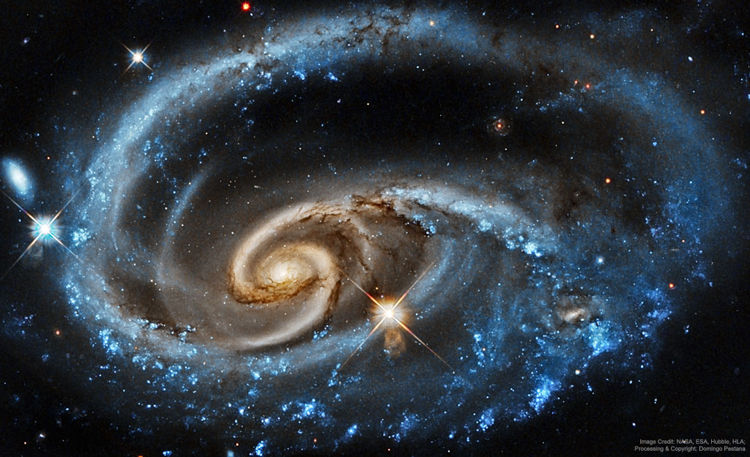 Die Galaxie UGP 1810 im Sternbild Andromeda hat wild geschlungene Spiralarme. In der Mitte sind das Zentrum und die Spiralarme gelb, außen herum blau und teilweise fleckig.