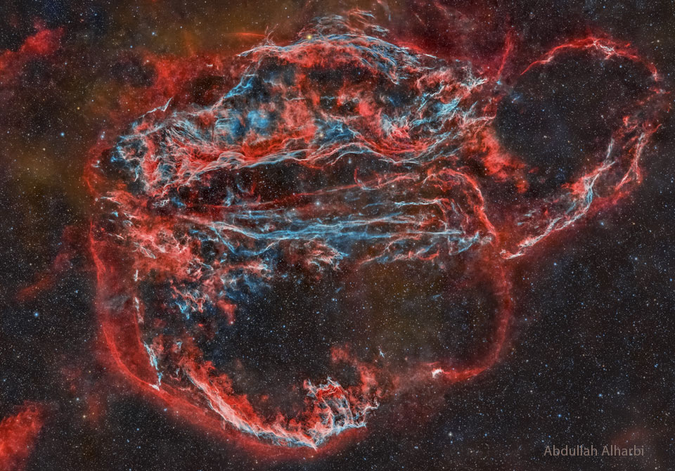 Am Nachthimmel ist eine große, komplexe Nebelwolke in Rot und Blau. Der Schleiernebel hat mehrere bekannte Teile, zum Beispiel den Fledermausnebel und den Hexenbesen.