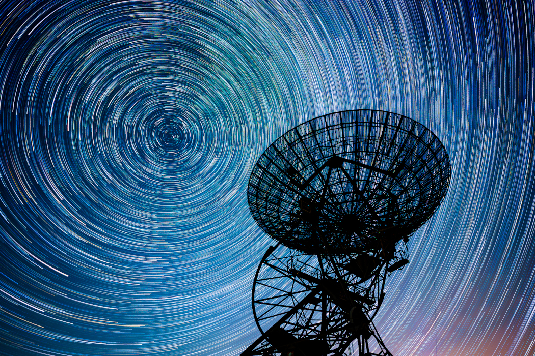 Hinter der Silhouette des One-Mile Telescope ziehen die Sterne leuchtende Spuren am Himmel.