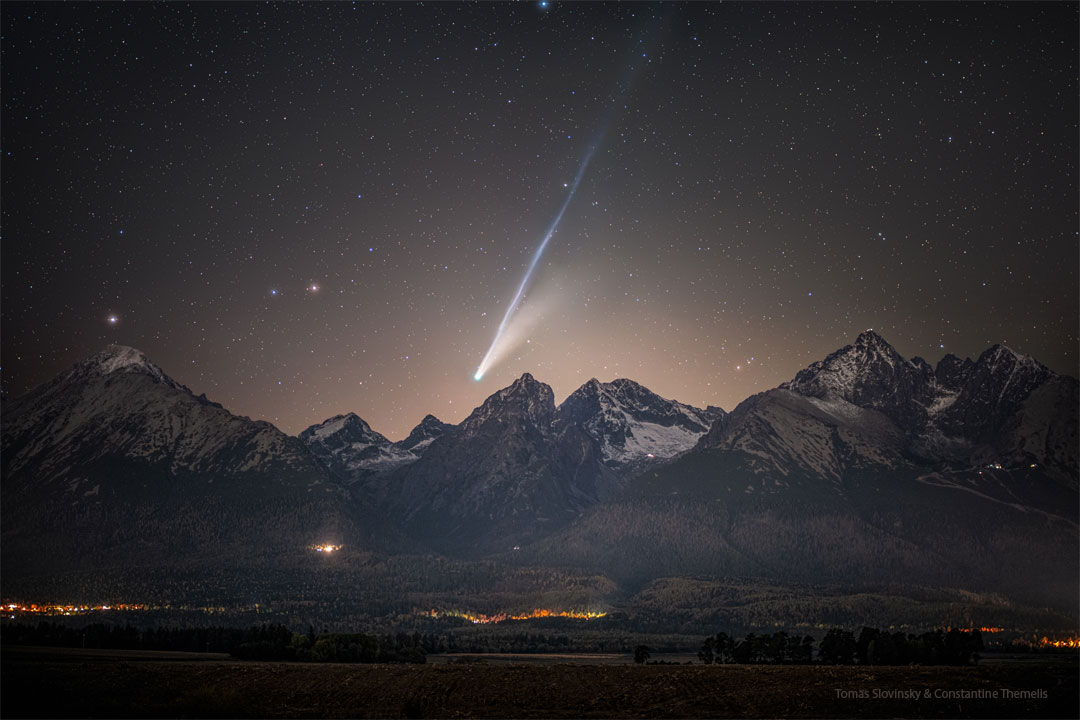 Vorne ragt eine Bergkette auf. Darüber ist der ein heller Komet zu sehen. Der Komet hat lange, helle Schweife, der der längere Schweif schimmert hellblau.