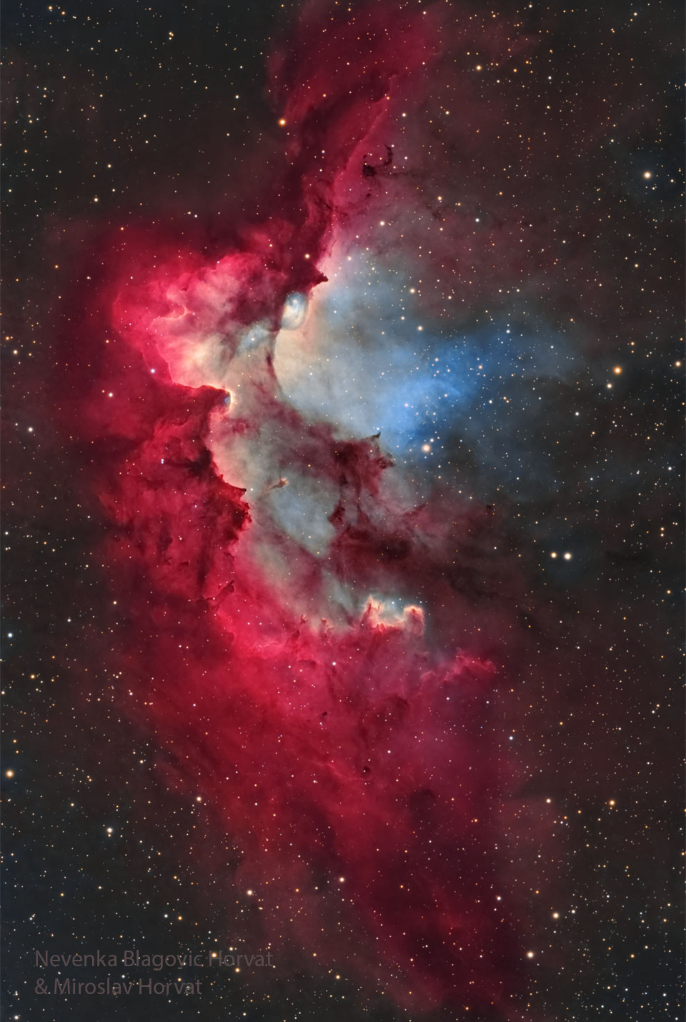 Die leuchtend rote Nebelgestalt hinter zart verteilten Sternen erinnert manche an einen Hexer mit spitzem Hut. Rechts hinter den dichten Wolken leuchtet eine bläuliche Region.