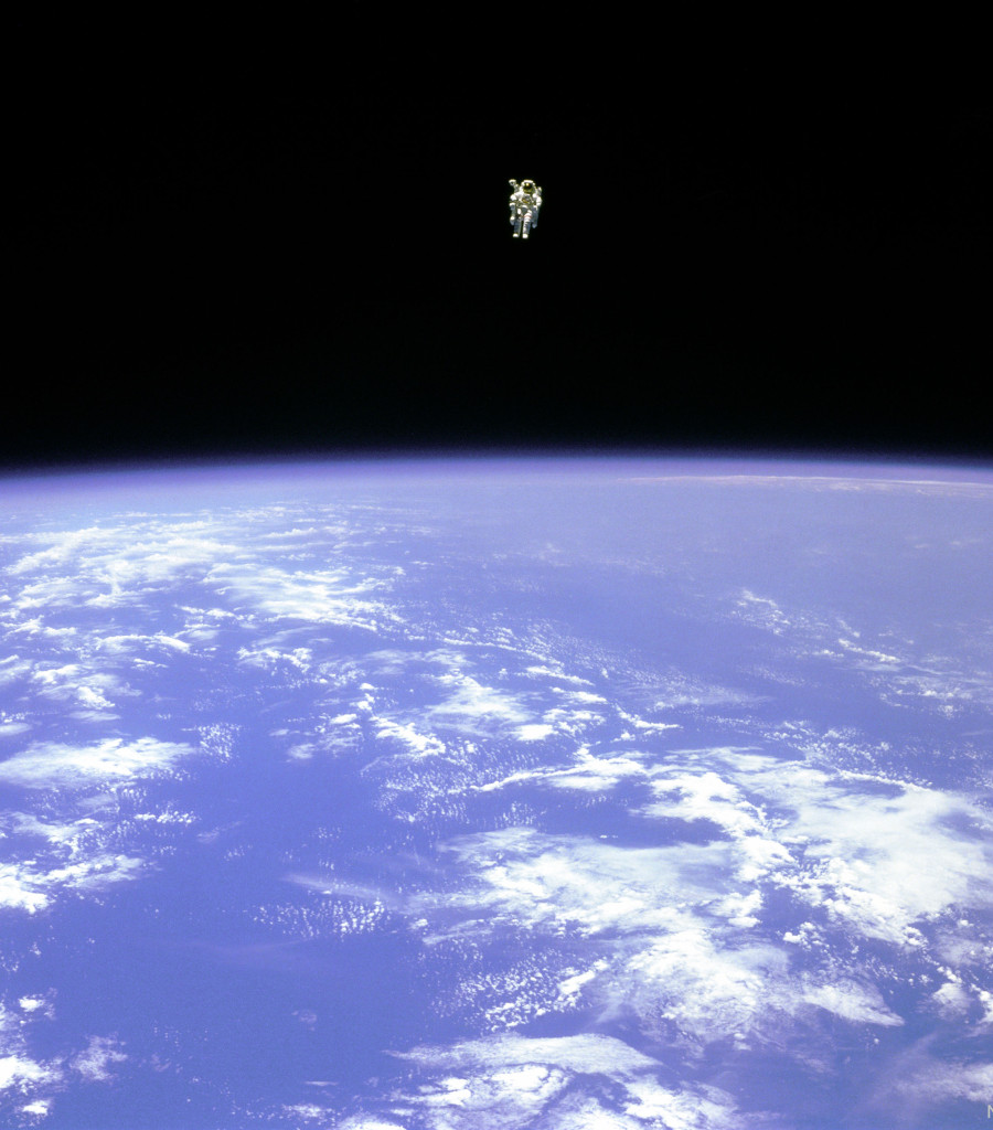 Über der blauen Erde mit weißen Wolken schwebt ein weit entfernter Astronaut im schwarzen All. Es ist Bruce McCandless II mit einer Manned Maneuvering Unit.