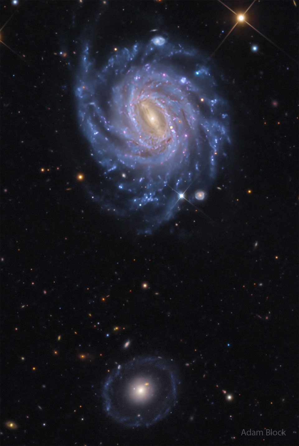In diesem Sternenfeld liegen zwei markante Galaxien. Oben ist eine helle Spiralgalaxie mit mehreren blauen Spiralarmen und einer Supernova. Unten ist eine blassere, runde Galaxie mit einem hellen Zentrum, die zwei Ringe aus Sternen hat.