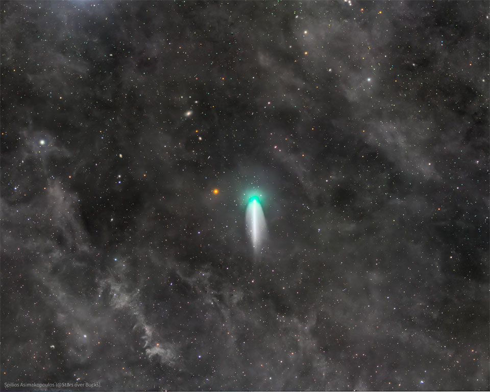 Vor einem Hintergrund mit blassen Nebeln und dünn verteilten Sternen protzt der Komet McNaught mit einer grünlichen Koma und einem breiten Schweif, der in der Mitte einen geraden hellen Streifen hat.