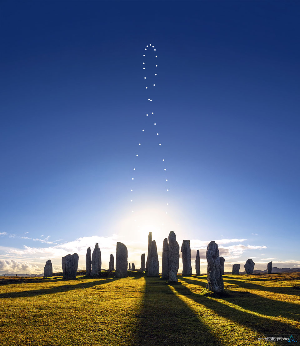 Die Sonne zieht eine 8-förmige Schleife am Himmel über dem Steinkreis von Callanish. Die senkrecht aufgestellten riesigen Steine werfen lange Schatten auf den Rasen davor.