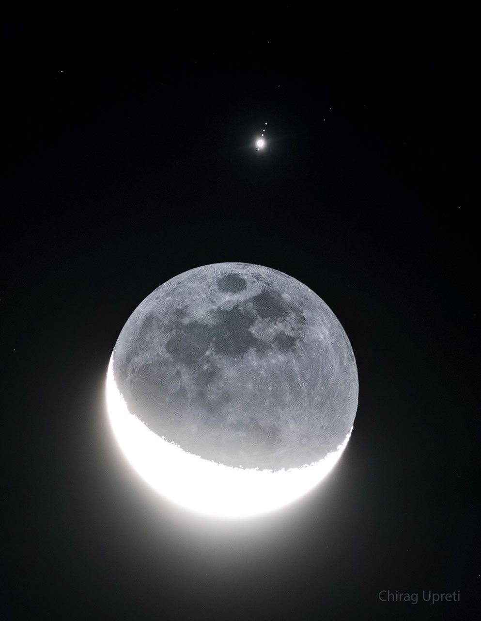 Über dem riesigen Mond strahlt der helle Jupiter mit seinen vier galileischen Monden. Die Nachtseite des Mondes wird von der Erde beleuchtet, daher erkennt man Meere und Strahlen um den Krater Tycho.