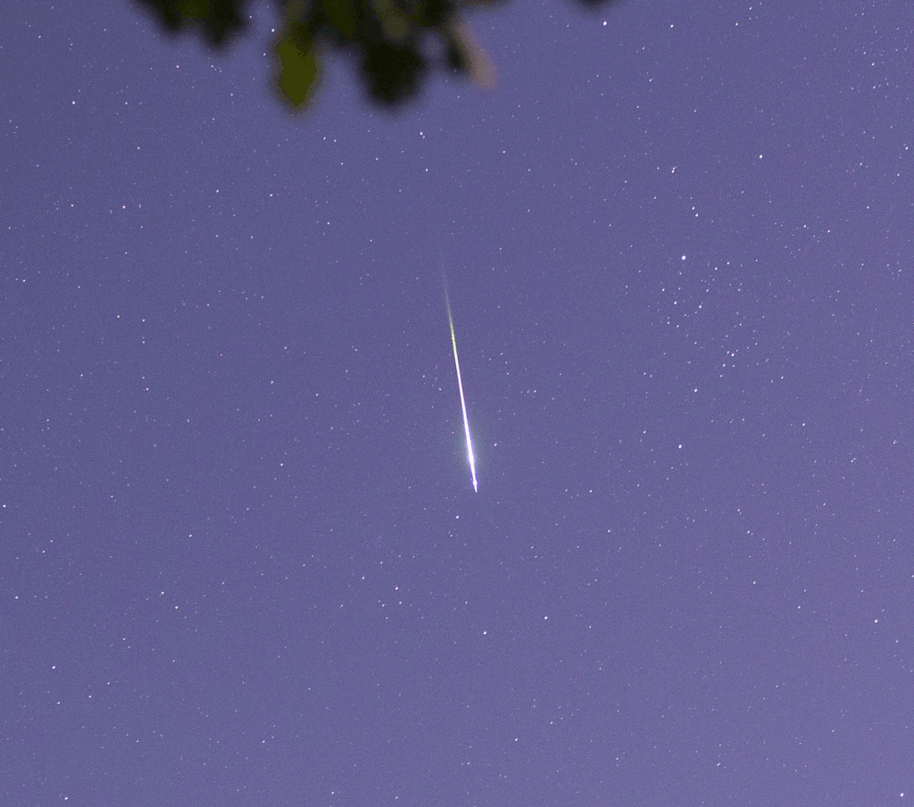 Ein Meteor zischt von oben über den Himmel in der Dämmerung und hinterlässt eine Rauchspur, die rasch verweht.